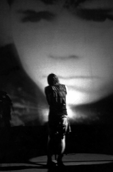 A shot from behind Trent, he's solo onstage black and white with the huge film of the kid from the Hurt video transposed in front of him