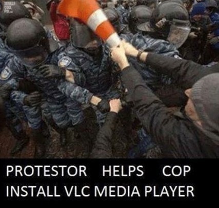 Meme "protestor helps cop install VLC media player" - he's hitting a cop on the head with a traffic cone