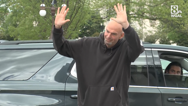 Photo of Fetterman holding arms aloft in front of vehicle