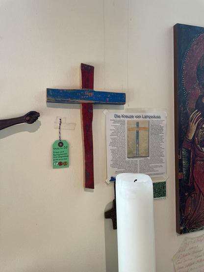 Im Vordergrund eine erloschene Altarkerze, an der Wand das Holzkreuz aus blauem und rotem holz 