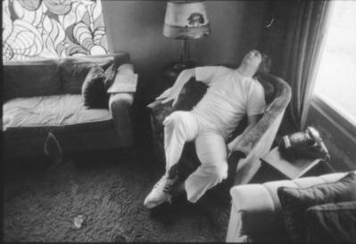 A photo of Brian Wilson reclining at home in the 60s with the Wild Honey stained glass in back, black & white