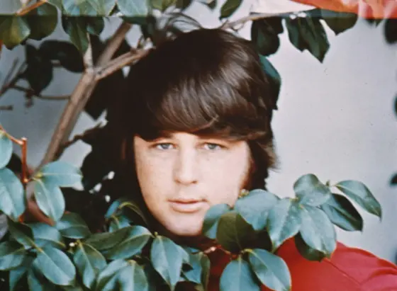 A photo of Brian Wilson looking out from behind some plants, color