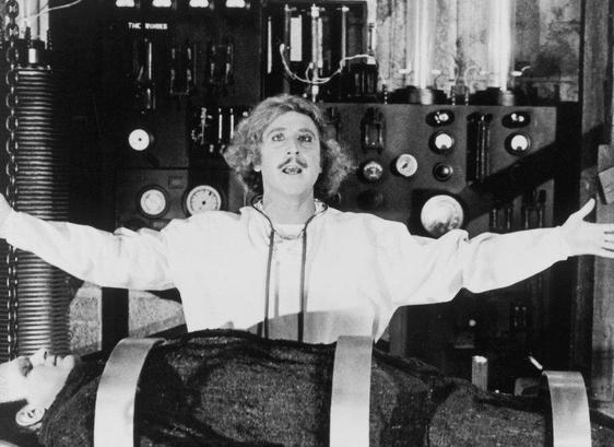 A still from Young Frankenstein (in black and white) where Gene Wilder as Dr. Frankenstein maniacally raises his arms in his laboratory above his monster, on the table (played by Peter Boyle)