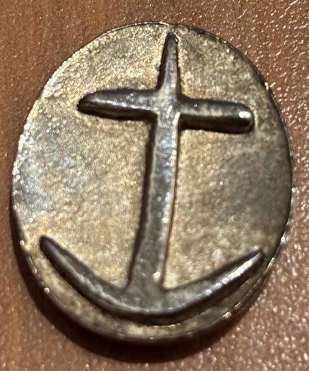Einen Segensmünze aus Metall, die einen Anker zeigt, der oben ein Kreuz formt. Aus dem Logo der deutschen Seemannsmission.