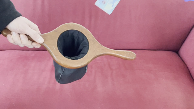 Über einem roten Sofa hält eine Hand einen schwarzen kollektenbeutel und eine andere Hand tut einen 20 Euro hinein 